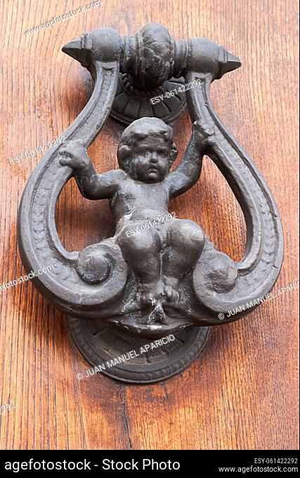 Old wrought iron knocker representing a child sitting on a swing on a wooden door