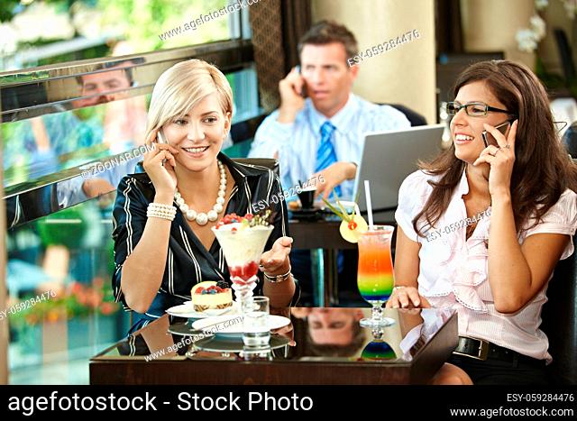 Young women sitting in cafe having sweets, talking on mobile phone