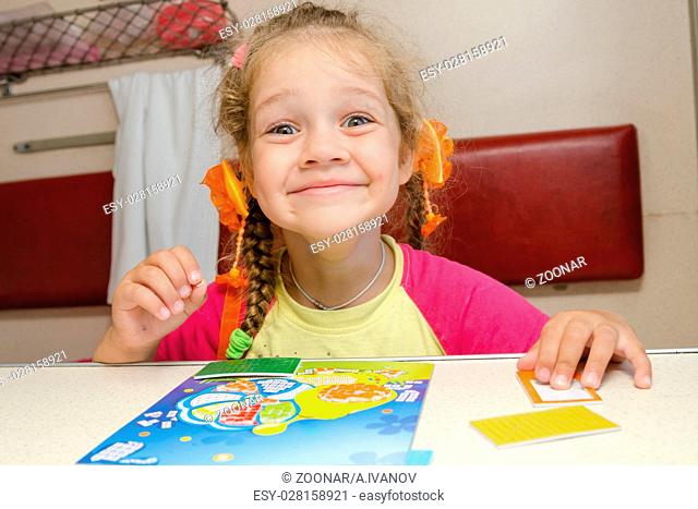 Little girl on the train with a happy smile sitting at a table on the lower second-class place car and makes the applique