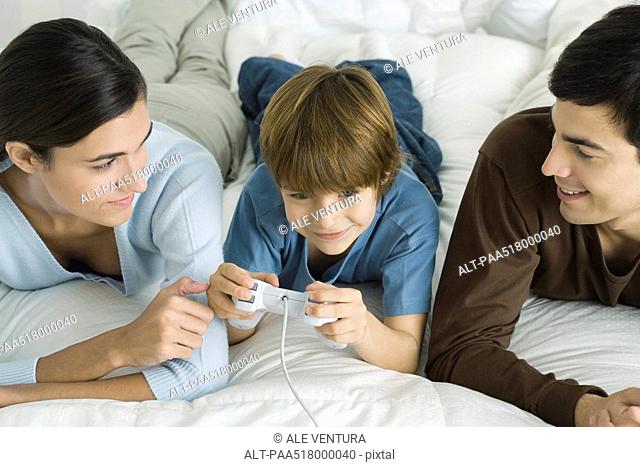 Family lying together on bed, boy playing video game