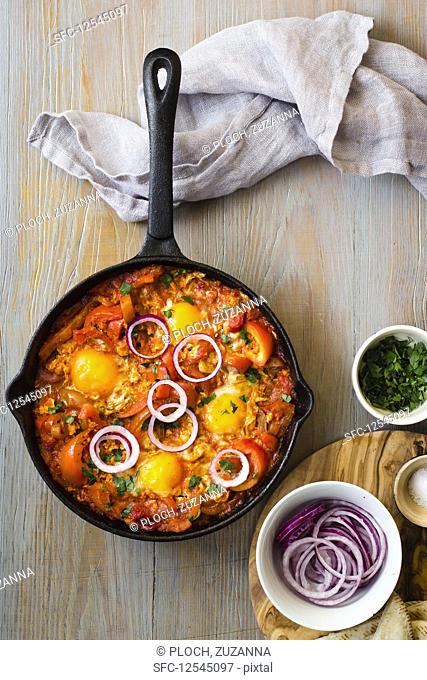 Shakshouka with peppers and tomatoes, chopped parley, rings of red onion and salt