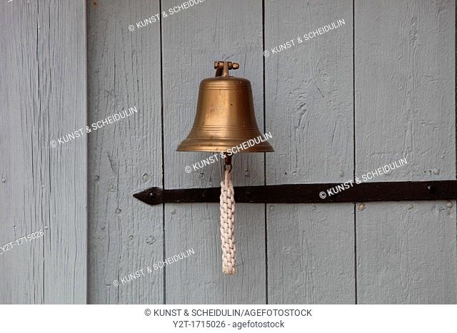 A small ship's bell hanging on a white wooden door