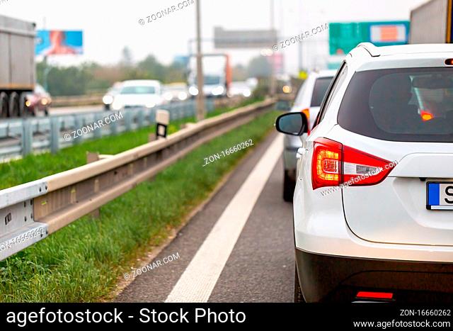 White car waiting in traffic jam on highway in rush hour. Automobile stuck on crowded road in evening. Vehicles in line with illuminated brake lights on full...