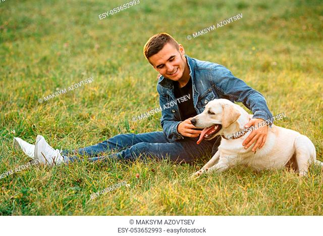 Smiling man sitting on grass with his dog labrador in park