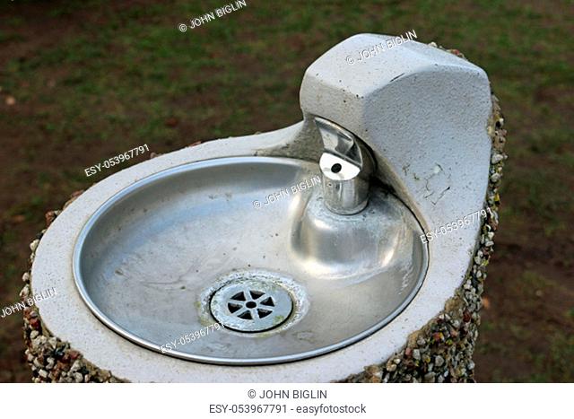 Metal park drinking fountain with bowl on a concrete plinth with a pebble dashed exterior