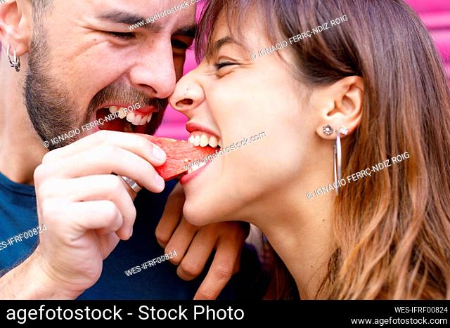 Cheerful boyfriend feeding watermelon to girlfriend