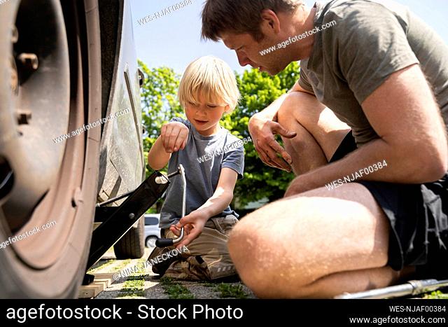 Father and son changing car tire in yard