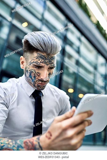 Young businessman with tattooed face, using digital tablet
