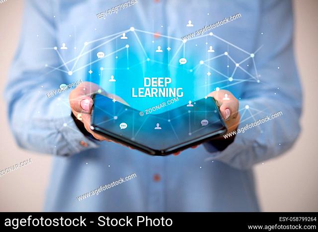 Businessman holding a foldable smartphone with DEEP LEARNING inscription, new technology concept