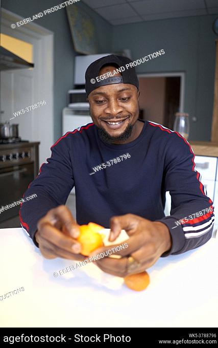 African man eating orange in kitchen