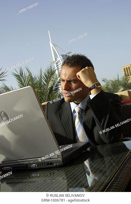 Thinking businessman working on laptop in Dubai (Burj Al Arab hotel in background)