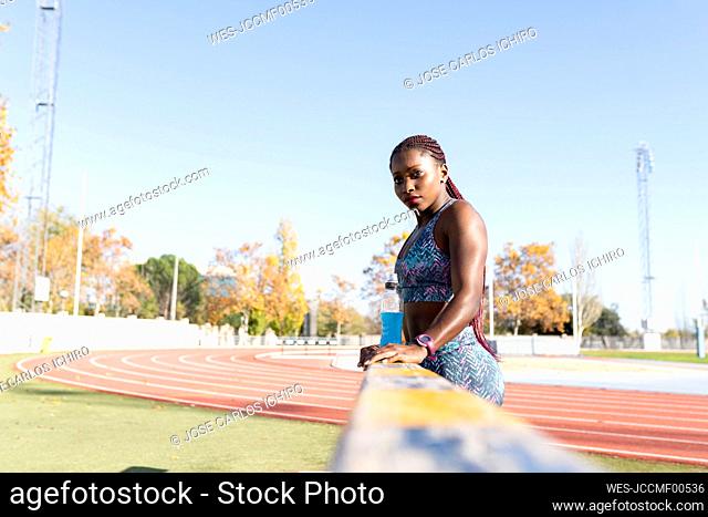 Sportswoman with energy drink standing by balance beam on sunny day