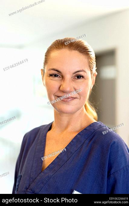 Vertical portrait of smiling caucasian female healthcare worker in corridor, with copy space