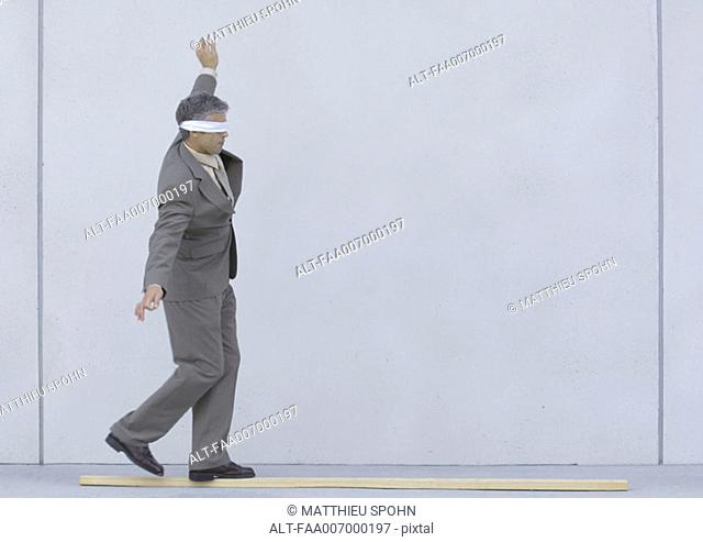 Blindfolded businessman walking on wooden plank