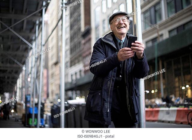 Man leaning against lamppost holding smartphone laughing, Manhattan, New York, USA