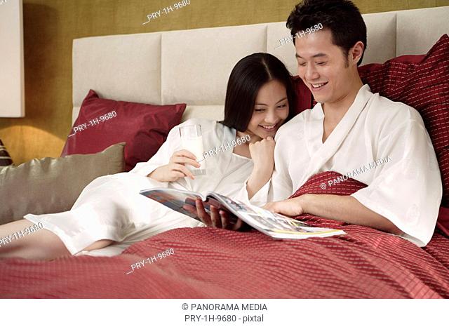 Young man sitting on bed with wife and reading magazine