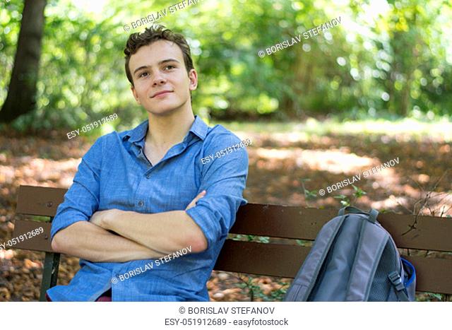 Young man day dreaming on a wooden bench in the park