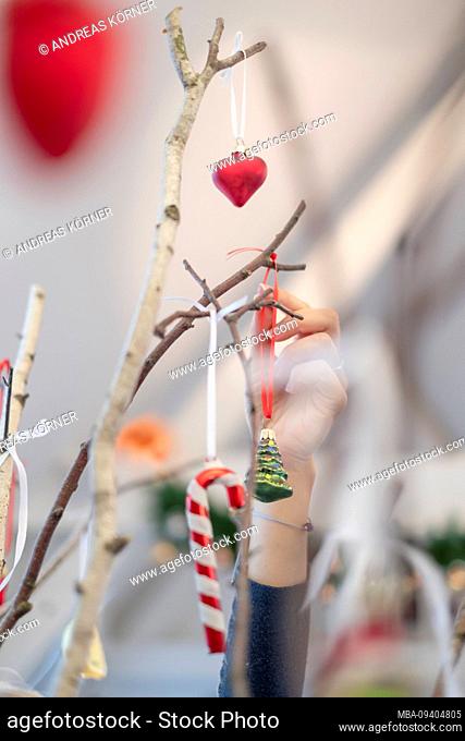 A woman hand decorates birch branches with Christmas decoration, heart glass ball