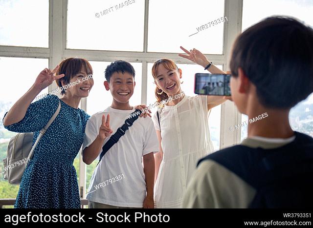 A boy using his mobile phone to take a picture of three Japanese people, a 13 year old boy, his mother and a friend