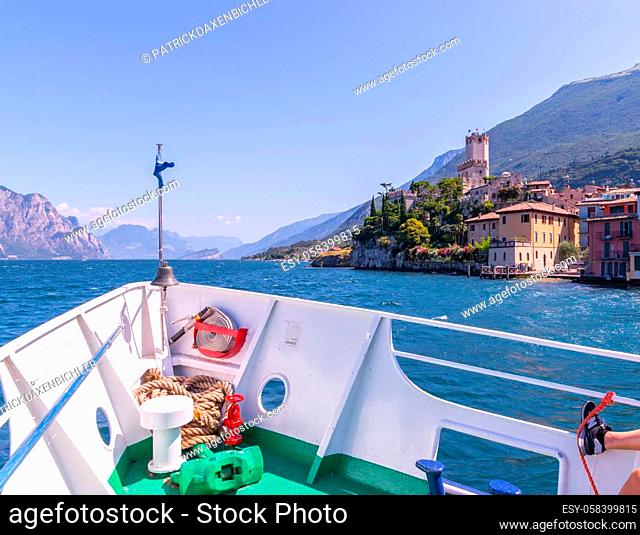 Bow of a boat on a boat tour. Blue water, mountain range and little village, Lago di Garda, Italy