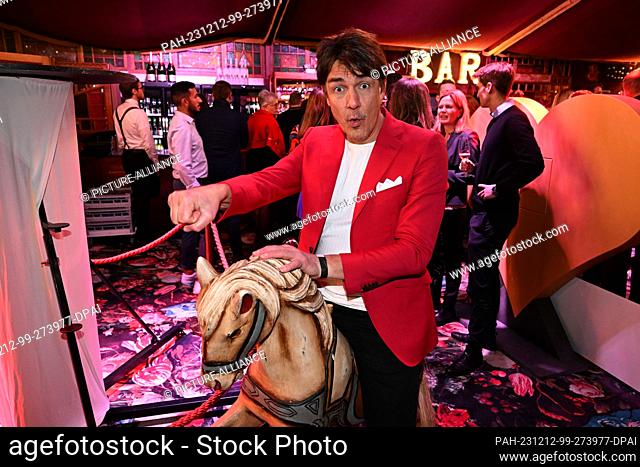 12 December 2023, Bavaria, Munich: Comedian Matze Knop sits on a wooden horse at Cathy Hummels' charity Christmas event in the Teatro Spiegel tent