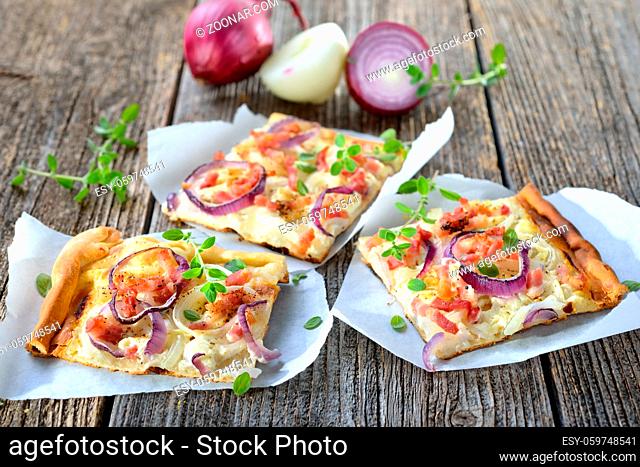 Streetfood: Klassische Elsässer Flammkuchen-Schnitten mit Zwiebeln und Speck auf Butterbrotpapier serviert - Hot baked tarte flambee from Alsace with onions