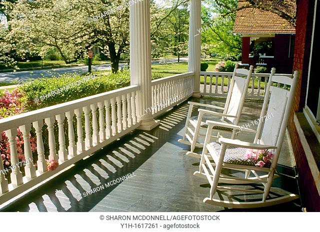 Two rocking chairs sit on wide front porch looking out over spring street blooming with dogwood, azaleas, and pears, Georgia, USA