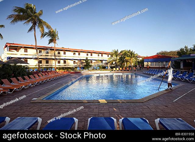 Man cleaning swimming pool, sun lounger, behind hotel building, parasol, coconut palm (Cocos nucifera), Hotel Club Amigo Costasur, Trinidad, Trinidad Province