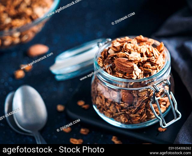 Homemade granola in glass jar on dark table. Ingredients for healthy breakfast. Copy space for text. Low key. Selective focus. Shallow DOF