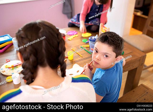 Portrait cute boy with Down Syndrome coloring at table with siblings