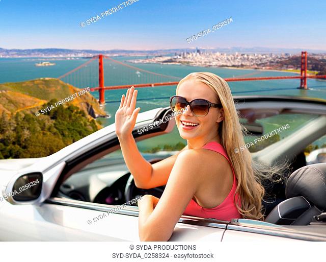 happy young woman in convertible car waving hand