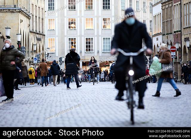 04 December 2020, North Rhine-Westphalia, Münster: People with mouth-nose protection walk and drive across the Prinzipalmarkt