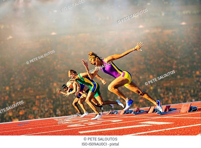 Four female athletes on athletics track, leaving starting blocks