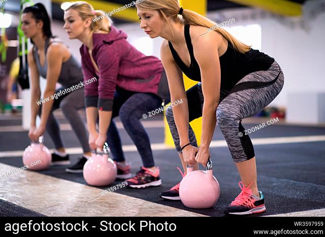 group of healthy young athletes doing exercises with kettlebells at cross fitness studio