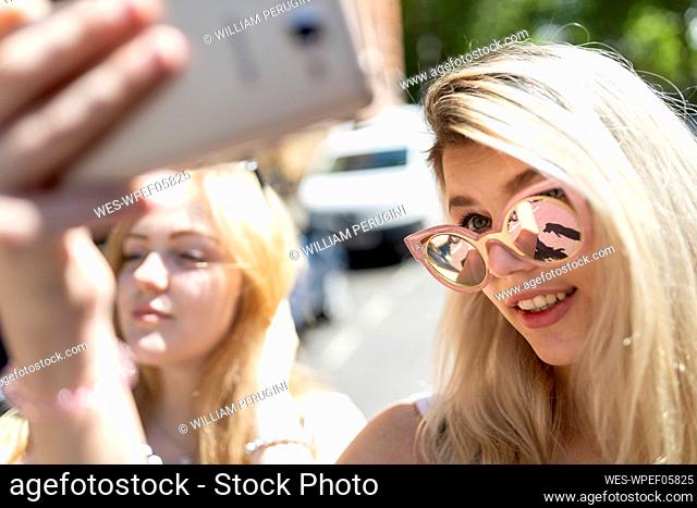 Smiling teenage girl wearing sunglasses taking selfie through mobile phone on sunny day