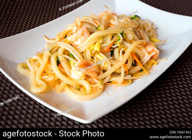 delicious japanese food yaki udon, noodles with seafood, shrips and vegetables, white plate on dark backgroung