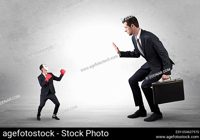 Big businessman being afraid of small masked businessman with box gloves in an empty room concept