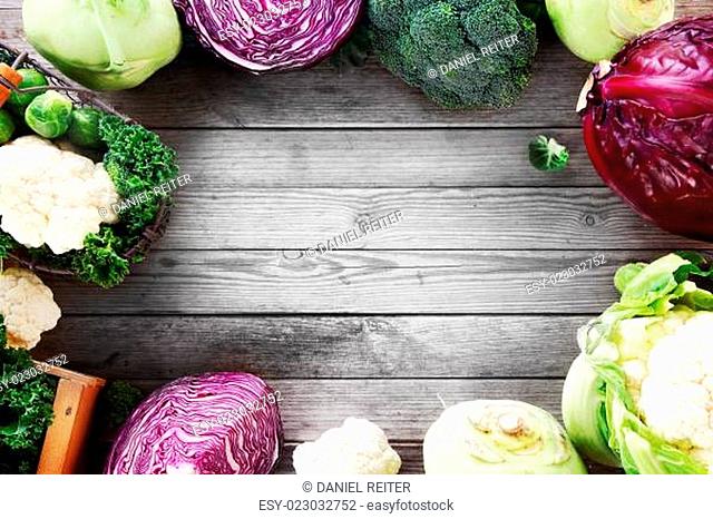 Frame of various brassica cabbage family varieties with cauliflower, kohlrabi, kale, cabbage and brussels sprouts over a rustic wooden background with copyspace