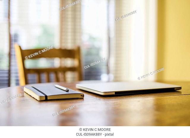 Notebook pen and laptop on dining room table