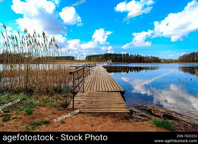 View of wooden pier inside lake, scenic view of reflection of the clouds and trees on lake, with cloudy blue sky background
