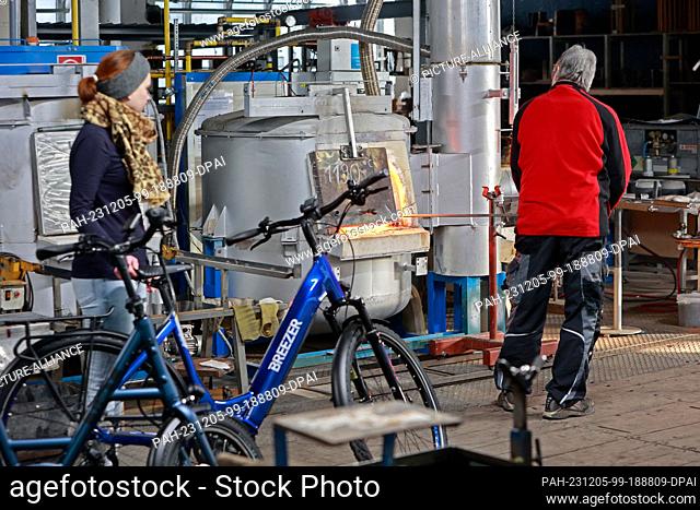 05 December 2023, Saxony-Anhalt, Derenburg: A visitor on a bicycle stands in front of the furnace where a glassblower is working at the Harz glass factory in...