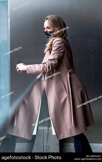 Thoughtful businesswoman looking away while leaning on railing during pandemic