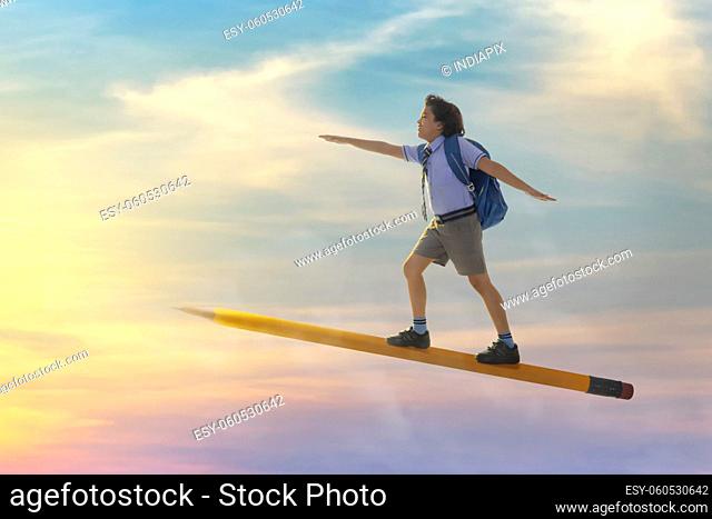portrait of a boy in school uniform flying on pencil in the sky