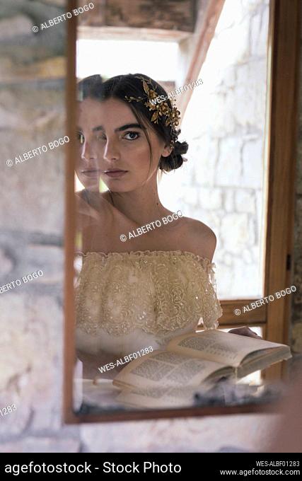 Young woman in wedding dress with book looking at mirror