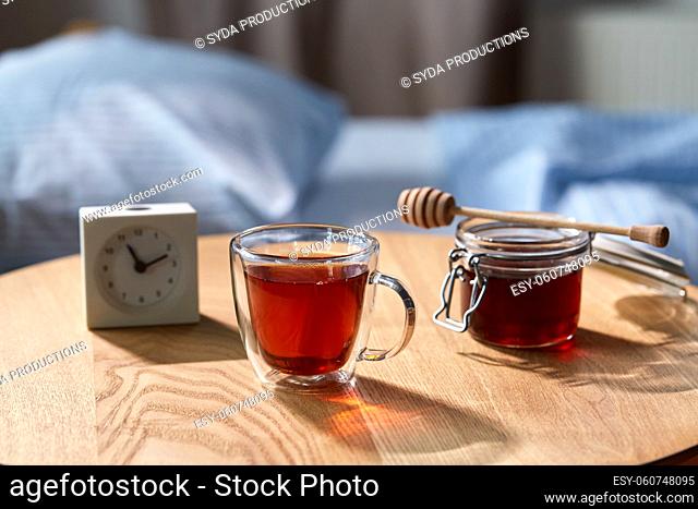 cup of tea, honey and alarm clock on table