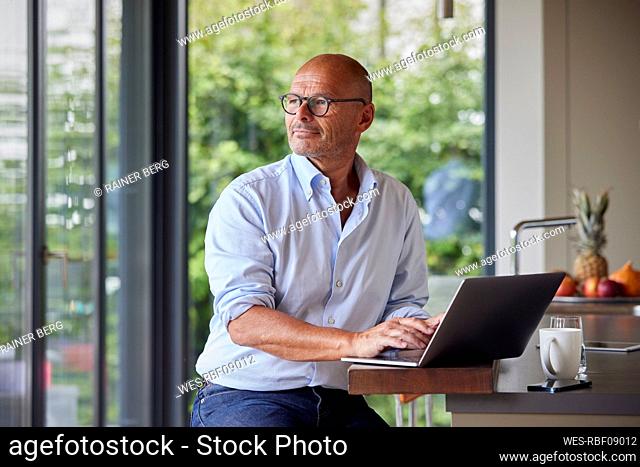 Thoughtful man with laptop sitting at kitchen island