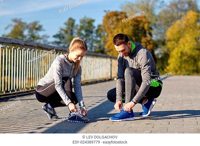 fitness, sport, people and lifestyle concept - smiling couple tying shoelaces outdoors