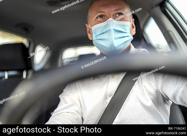 A man in a protective mask driving a car, steering wheel in the foreground, Portugal, Europe