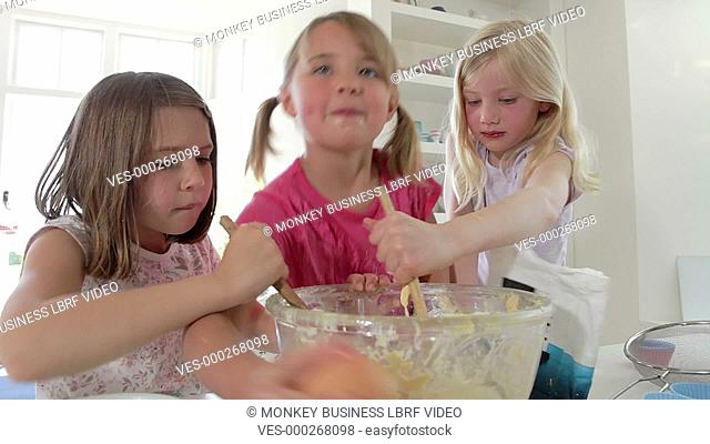 Three young girls adding ingredients into glass mixing bowl to make cake.Shot on Canon 5D Mk2 at a frame rate of 25fps