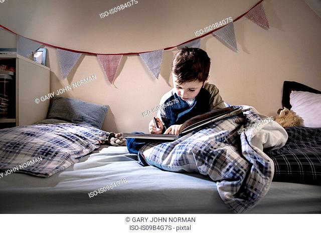 Boy sitting in bed reading book by torchlight